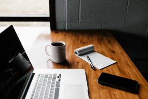 desk with mac, phone, notepad, and coffee